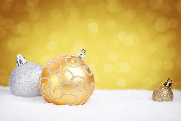 Gold and silver Christmas baubles on snow, gold background