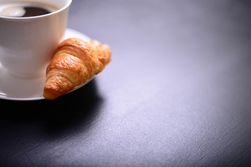 Fresh coffee and croissant on black background