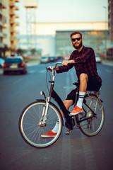Fototapeta na wymiar Stylish man in sunglasses riding a bike on city street