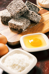 Group of Lamingtons on a timber cutting board with food ingredients in the backgrou