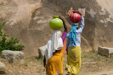Two Indian women carry water on their heads in  pots 