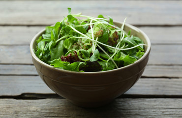 Fresh mixed green salad in bowl on wooden table close up