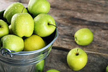 Ripe green apple in metal bucket on wooden table close up