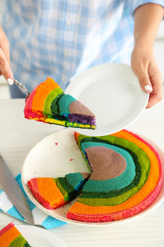 Young woman cutting rainbow cake in kitchen