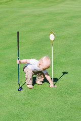 Cute little baby boy playing golf on a field