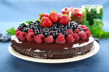 Delicious chocolate cake with summer berries on blue tablecloth background