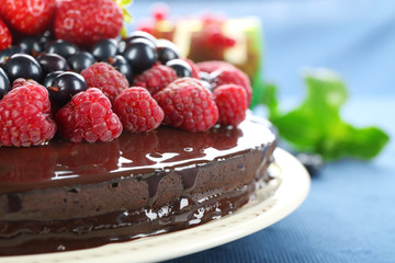 Delicious chocolate cake with summer berries on blue tablecloth, closeup