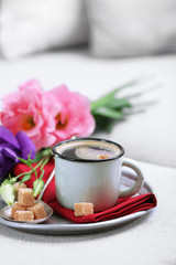 Cup of coffee with flowers on tray on sofa in room