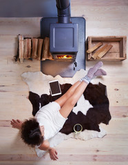 Young woman with cup of coffee sitting home on a cow rug by the fireplace. Fall winter relaxing and leisure concept. - 91930199