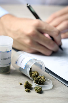 Doctor writing on prescription blank and bottle with medical cannabis on table close up