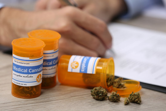 Doctor Writing On Prescription Blank And Bottle With Medical Cannabis On Table Close Up