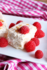Sweet nougat with nuts and raspberries on plate close up