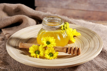 Honey with flowers and dipper on wooden tray on table