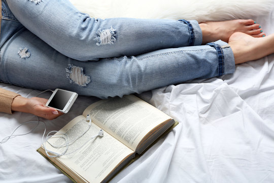 Woman in blue jeans watching phone on bed top view point