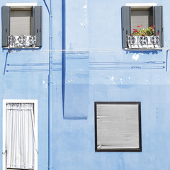 Blue painted wall with several windows with green wooden shutters, at the island of Burano, Venice, Italy