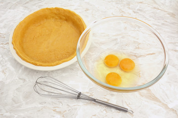 Bowl of eggs with a whisk and lined pie dish