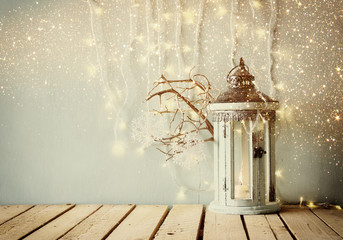 Fototapeta premium white wooden vintage lantern with burning candle and tree branches on wooden table. retro filtered image with glitter overlay 