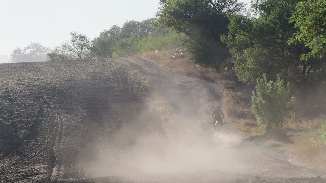 Enduro racer riding motorcycle on dirt track kicking up dust long shot