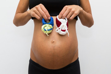 eine schwangere Frau hat Babyschuhe vor dem Bauch