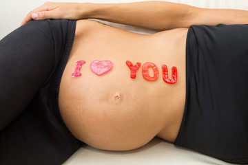 auf dem Bauch einer schwangeren Frau steht I love you, mit einem Herz