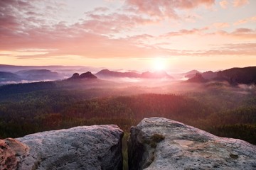 View over sandstone cliff into deep misty valley in Saxony Switzerland. Sandstone peaks increased from heavy foggy background.