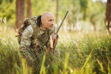 hunter with shotgun looking through binoculars in forest