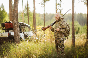 hunter with shotgun looking through binoculars in forest