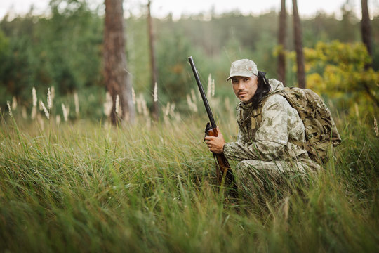 hunter with shotgun looking through binoculars in forest