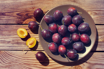 Fresh juicy plums in a round plate on a wooden surface. Crop of plums