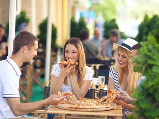 Foto op Canvas Four cheerful young friends sharing pizza in a outdoor cafe © bokan