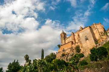 Obraz premium Sight from below of the Parochial Church of the Purest Conception with a blue sky and gray storm clouds. The church is in Zufre, mountain town of Huelva, Spain
