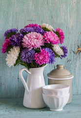 flowers asters in a white enameled pitcher and vintage crockery - ceramic bowl and enameled jar, on a blue wooden background. Vintage and rustic style
