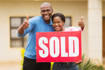 african couple outside home with sold sign - obrazy, fototapety, plakaty