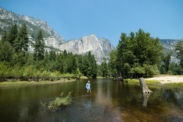 Man looking at idyllic view of Yosemite National Park valley during summer vacation on perfect day with clear blue sky surrounded by lush greenery and mountains