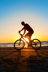 Obraz premium Man cyclist silhouette on blue sky and multicolored sunset backg