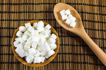 Sugar Cubes in Bowl and on Wooden Spoon over Wooden Background