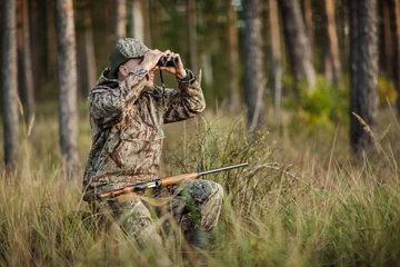 Crédence de cuisine en verre imprimé Chasser hunter with shotgun looking through binoculars in forest