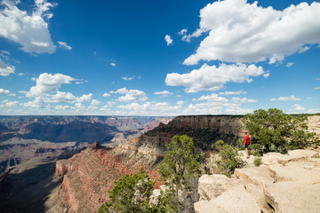 Man hiking overlooking epic view at the Grand Canyon National Park, Arizona, USA on a perfect Summer day with clear blue sky and puffy white clouds.