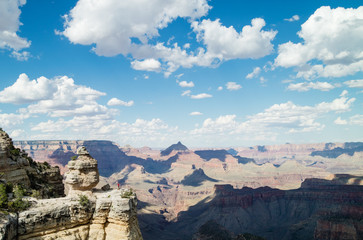 Man hiking overlooking epic view at the Grand Canyon National Park, Arizona, USA on a perfect Summer day with clear blue sky and puffy white clouds.