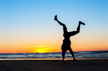 Fototapeta premium Young man making handstand on the beach. Multicolored sunset bac