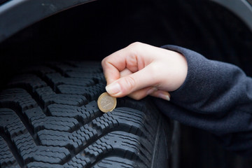 Frau misst Reifenprofil eines Autoreifen