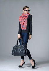 portrait of gorgeous young lady in sunglasses with bag on gray background