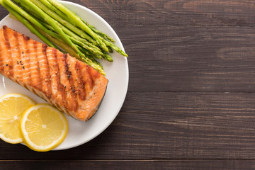 Grilled salmon with lemon, asparagus on the wooden background