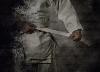 Foto auf Acrylglas Kampfkunst Karateka bindet den weißen Gürtel (Obi) mit Grunge-Hintergrund