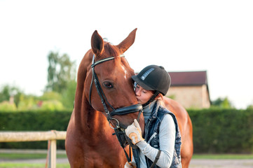 Young teenage girl equestrian kissing her chestnut horse.