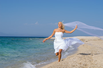 Fototapeta na wymiar Young bride in wedding drees having fun on the beach