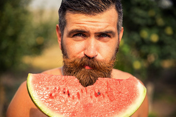 Happy brutal bearded man in the garden with juicy ripe watermelon