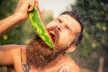 Happy brutal bearded man in the garden with juicy ripe watermelon