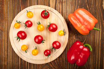 Cherry tomatoes on cutting board and peppers bell on wooden back