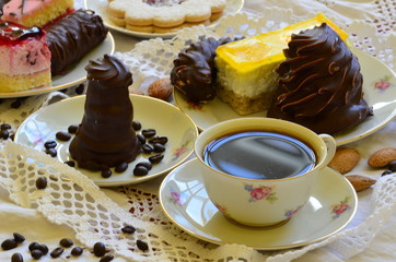 Desserts with cup of coffee, coffee beans and almonds on white tablecloth